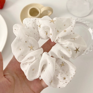 Close-up of white chiffon hair scrunchie with golden stars and dot patterns