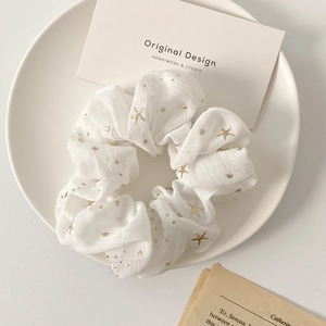 Detail view of cream chiffon scrunchie with gold star foil prints on a minimalist plate
