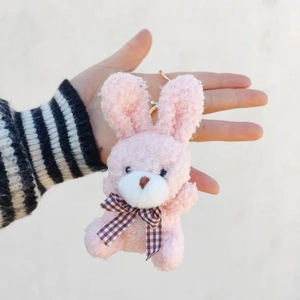 Close-up of a pink plush rabbit keychain with curly fur and a checkered bow tie detail