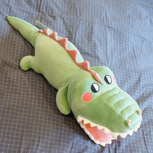 Cute green crocodile plush pillow for sleeping, soft stuffed toy on a grey checkered bed