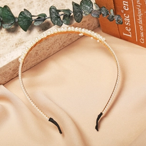 Detail of a thin gold metal headband with small white pearls and black non-slip tips