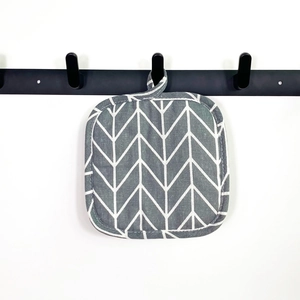 Thick square grey cotton trivet with geometric pattern hanging on a metal hook