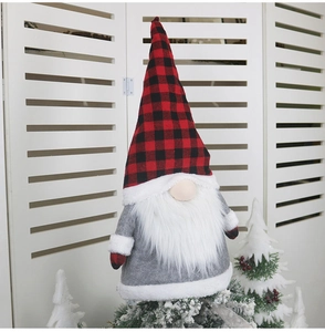 Detail showing a plush gnome tree topper with a red plaid hat on a snowy pine branch
