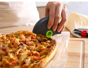 Action shot of dark grey circular pizza cutter slicing through a crust on wood board