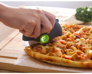 Close-up of a handheld circular pizza cutter slicing a fresh pizza on a wooden board