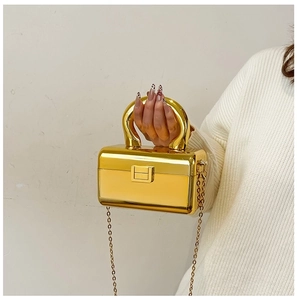 Detail of gold box clutch bag featuring thick circular handle and metallic chain strap