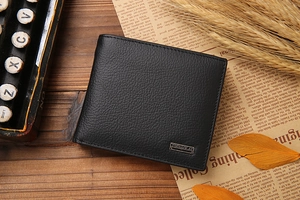 Close-up of black lychee leather bifold wallet with metal logo on vintage wood desk