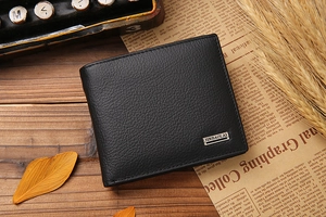 Close-up of black bifold leather wallet with lychee grain and metal logo on wood