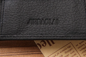 Macro shot of black litchi grain leather texture and embossed logo on short wallet