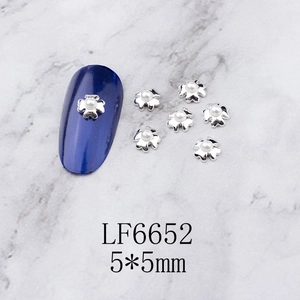 Detailed view of silver 5-petal flower nail charms with pearls on navy blue nail art