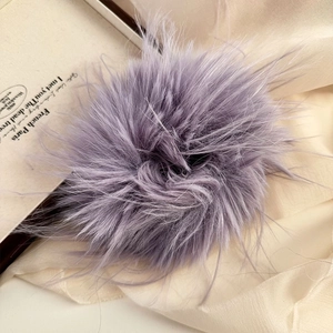 Close-up of a soft purple faux fur hair tie resting on elegant silk fabric background