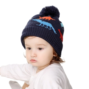 Close-up of baby knitted hat featuring colorful dinosaur patterns and a pom-pom top