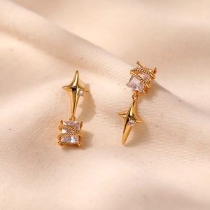 Macro shot of gold star-shaped earrings with square zircon stones on beige fabric