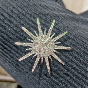 Vintage silver starburst brooch with sparkling rhinestones on black knit background