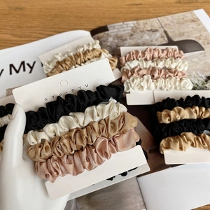 Set of four satin silk scrunchies in neutral earth tones on a retail display card