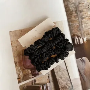 Close-up of black silk satin hair scrunchies on a nyu-nyu card with soft sheen texture