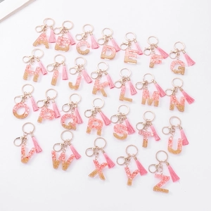 Pink resin alphabet keychains with gold flakes and tassels on a clean white background
