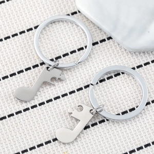 Matching stainless steel musical note keychains for couples on a textured background