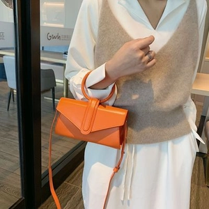 Detalle del bolso bandolera de cuero naranja brillante con asa circular y solapa