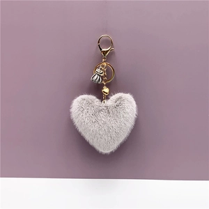 Close-up of grey heart-shaped plush keychain with golden lobster clasp and flower detail