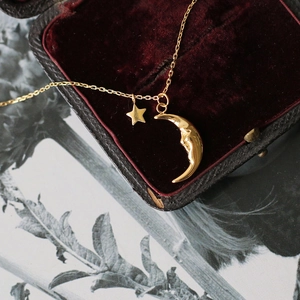 Detail of 18K gold crescent moon and star pendant necklace on red velvet box