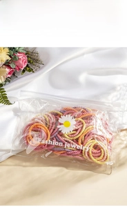Detail of macaron hair elastics set in daisy zip bag on white silk with flowers