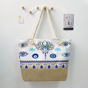 Detail of canvas tote bag with thick rope handles and blue evil eye graphic