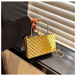 Detailed shot of golden evening clutch with V-shaped texture and faux pearl clasp