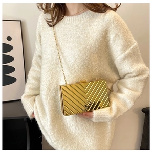 Chic gold clutch bag with V-shaped texture and chain strap worn by a model in white