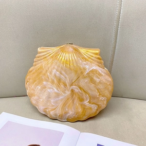 Detail of shell-shaped evening clutch in amber and cream resin with marble texture