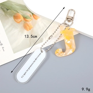 Macro view of a yellow marble acrylic letter J keychain with French text charm and silver clasp