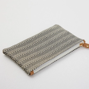 Minimalist black and white woven straw clutch bag with brown leather zipper pull tab