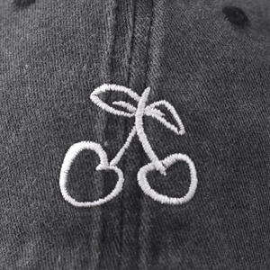 Close-up of white cherry embroidery on dark grey washed cotton baseball cap fabric