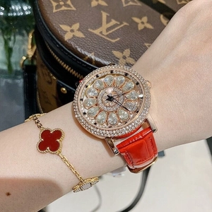 Detail of luxury rotating floral diamond watch with red leather strap and clover bracelet