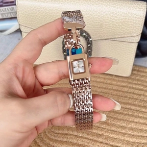 Close-up of a luxury rose gold rectangular padlock watch held against a beige handbag