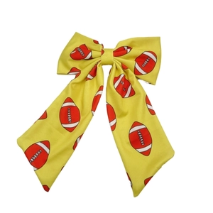 Yellow Super Bowl hair bow clip with all-over football print patterns on white background