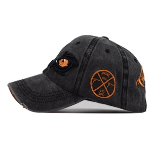 Detail of orange eyes embroidery on charcoal grey washed cotton baseball cap with vintage patch