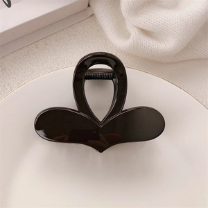 Close-up of a minimalist black bow hair claw clip placed on a white ceramic plate