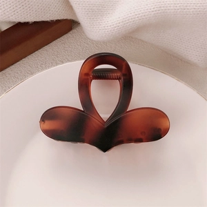 Brown tortoiseshell heart hair claw clip on a white ceramic plate with a cozy beige background