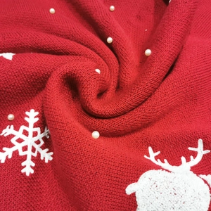Detail of red knit Christmas tree skirt with white reindeer embroidery and pearl accents