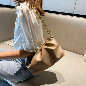 Close-up of beige ruched cloud pouch bag with thick golden chain strap on a model