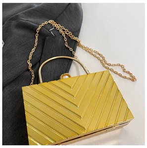 Close-up of golden rectangular evening clutch with geometric V-stripes and pearl clasp
