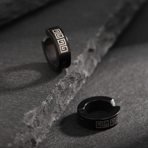Close-up of black titanium steel ear clips with Greek pattern on dark rock background
