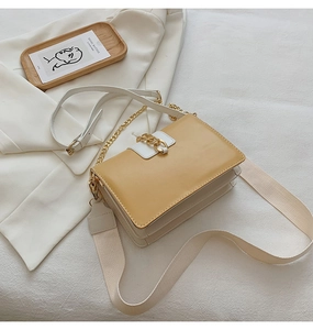 Detail of yellow and white crossbody bag with gold chain strap on white fabric