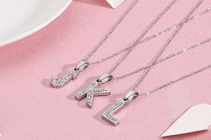 Gros plan des pendentifs J, K et L sertis de zircons blancs sur un fond rose doux