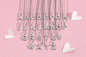 Gros plan de pendentifs lettres en argent sertis de zircons sur fond de cœurs roses
