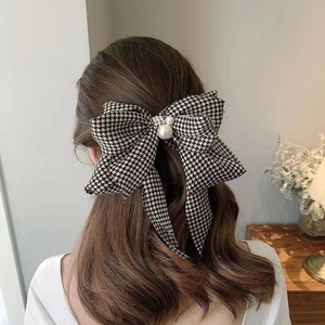 Detail of a black and white houndstooth bow hair clip with elegant pearl accents