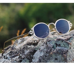 Detail of silver steampunk sunglasses with engraved cross patterns on a rock surface
