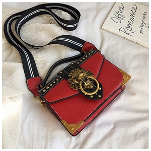 Detail of red square bag with vintage gold lion head and striped strap on white fabric