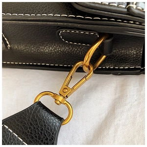 Close-up of black lychee grain leather handbag with white stitching and gold hardware hooks